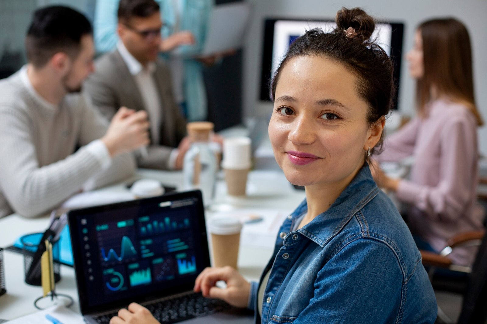 Mulher sorridente trabalhando em laptop com gráficos e indicadores de desempenho em reunião de equipe — conceito de gestão de dados, produtividade e tecnologia empresarial. Imagem de capa para o blogpost Conheça 3 motivos para você contratar BPO Financeiro