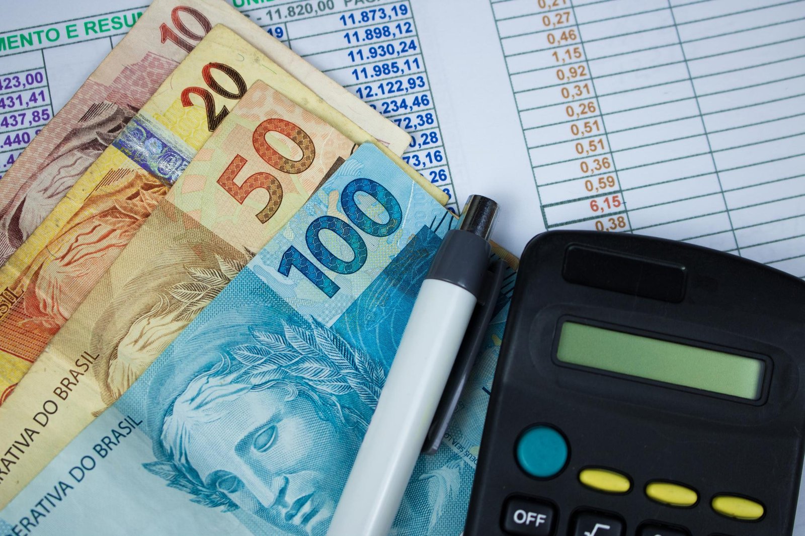 Notas de real de diferentes valores dispostas sobre planilhas financeiras, acompanhadas de uma caneta branca e uma calculadora preta. Imagem de capa para o blogpost Reforma Tributária 2026: O Guia Completo para Empresas e Empreendedores