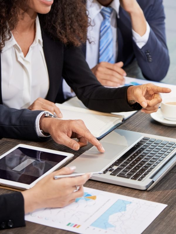 Faceless shot of coworking businesspeople surfing laptop while discussing project at table in office